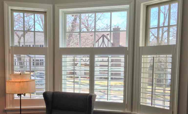 Half-length white shutters in family room bay window.